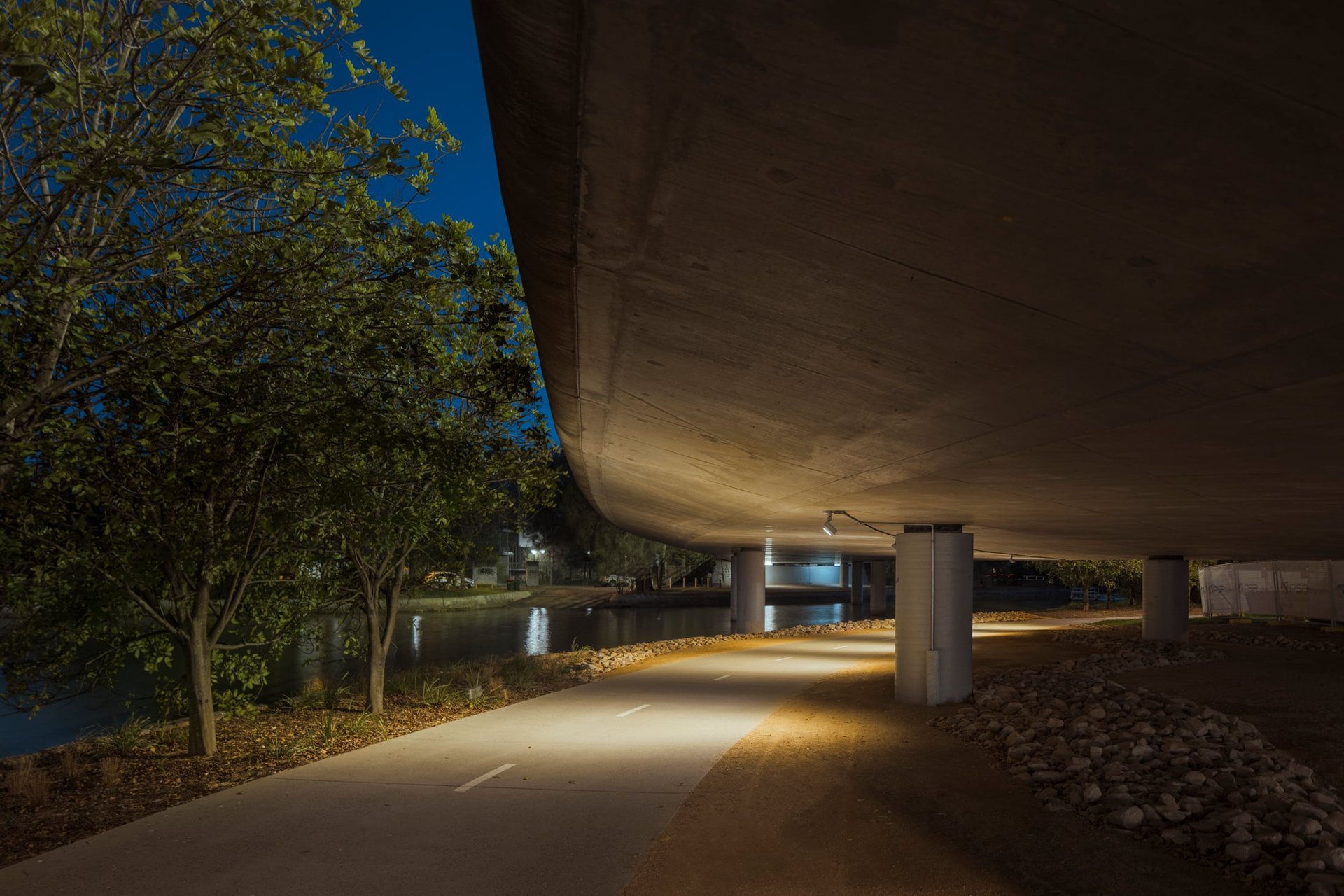 Bay Run path passing under a street bridge, with luminaires mounted beneath the bridge providing bright light to enhance safety for pedestrians and cyclists.
