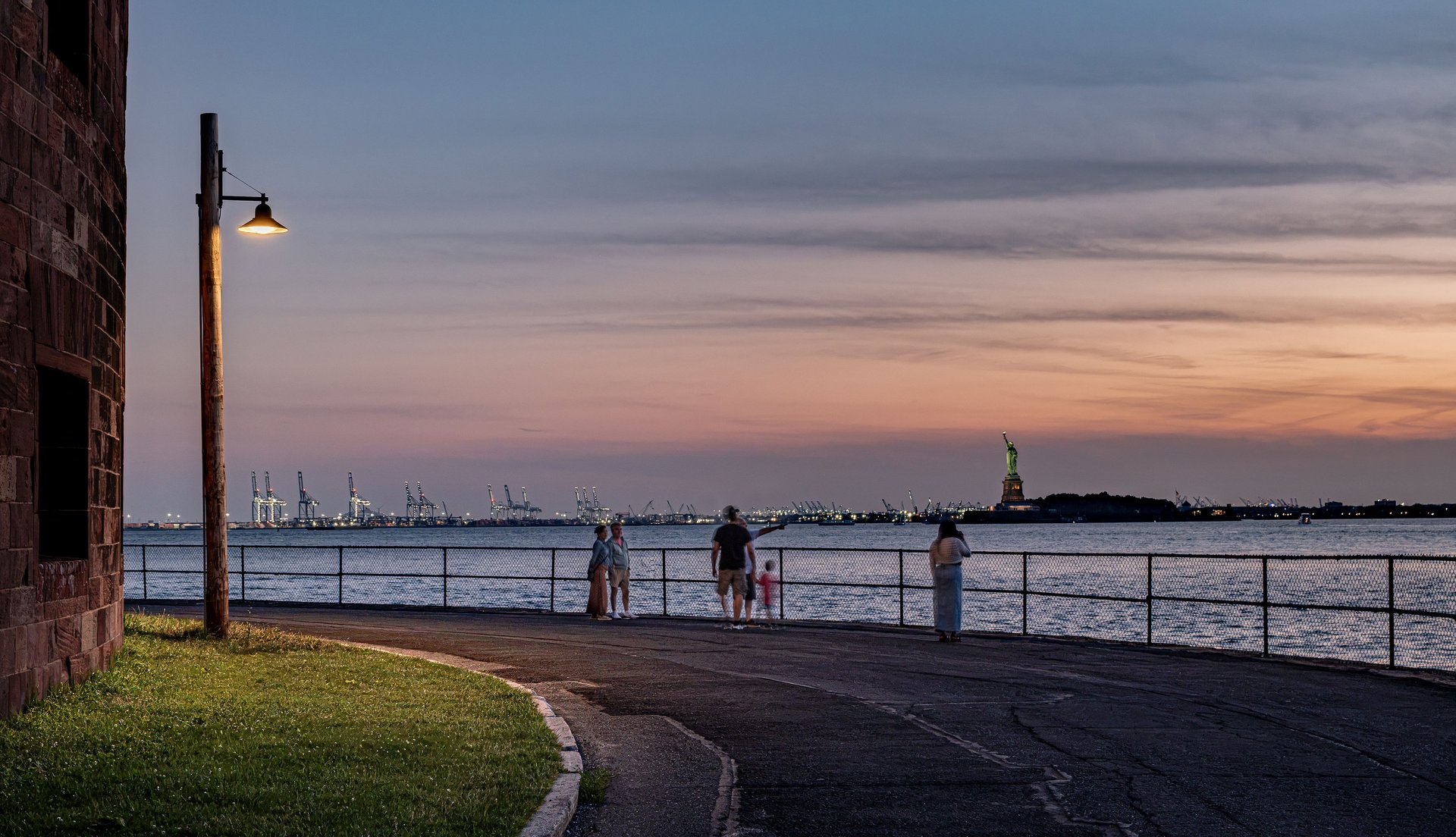 Promenade en bord de mer sur Governors Island, à New York, éclairée par un luminaire sur mât WE-EF, avec la statue de la Liberté au coucher du soleil