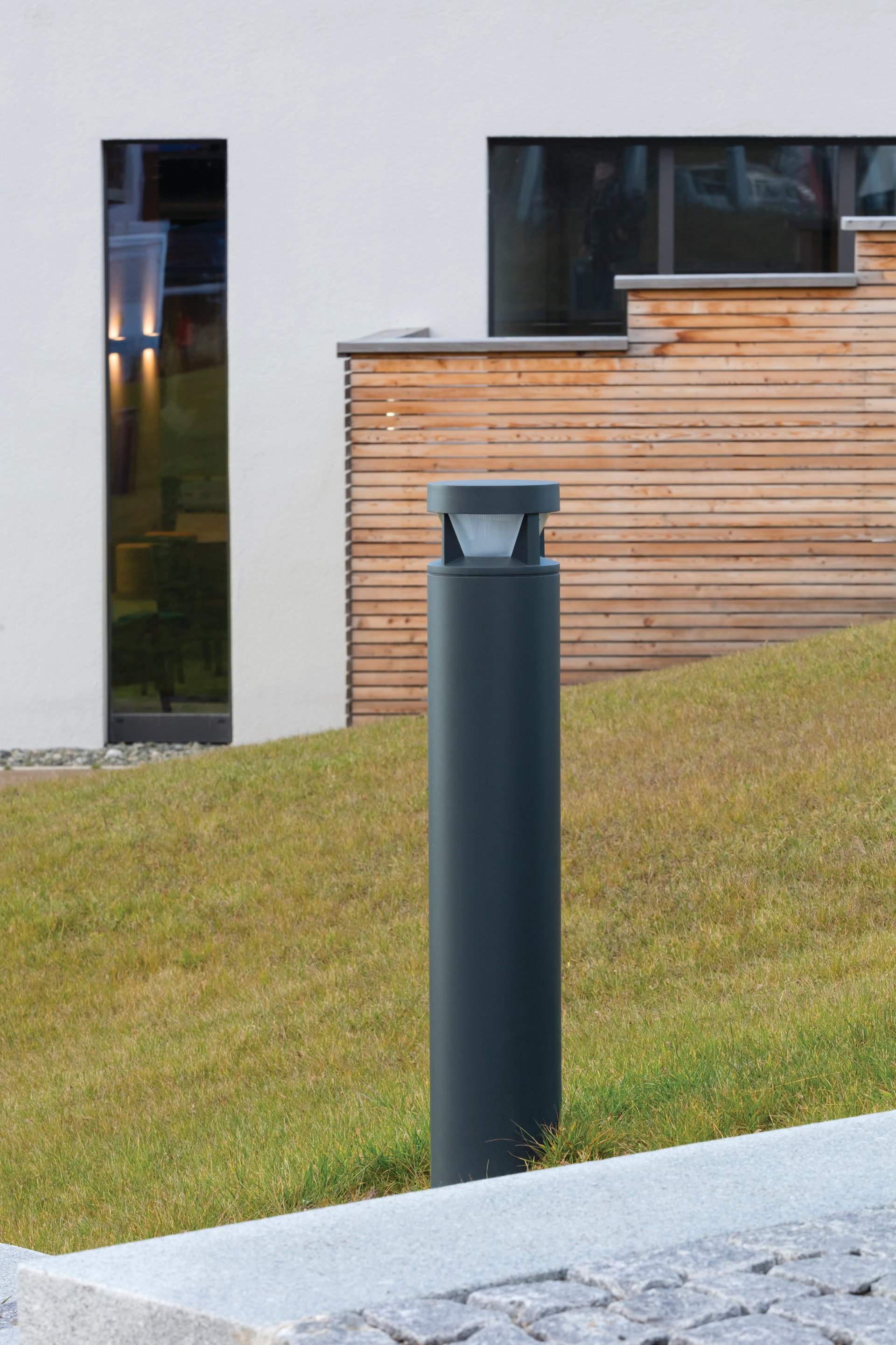 WE-EF KTY234 LED bollard providing glare-free pathway lighting at das flax Hotel in Dietmannsried, Allgäu, installed with large spacing intervals for efficient illumination of pedestrian walkways, contemporary design complementing light-colored clinker brick facade and wooden cladding elements of modern economy hotel designed by FG-Architektur Sonthofen emphasizing regional sustainability and bleisure travel concept