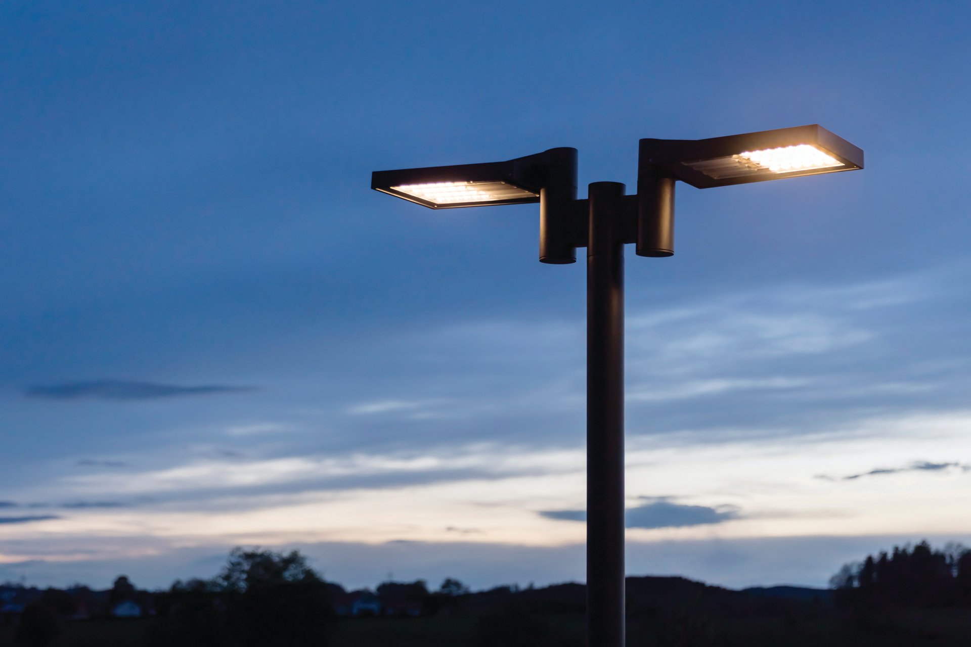 WE-EF VFL530 LED street luminaire on striking dual-arm pole at 4.5-meter height providing glare-free driveway illumination at das flax Hotel using asymmetric forward-throw wide-beam R65 optical distribution with warm white 3000K color temperature, contemporary luminaire design harmonizing with modern architecture of bleisure hotel complex in Allgäu region emphasizing regionality and welcoming atmosphere