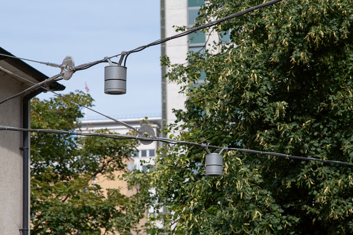Southern House Croydon connecting path from George Street showing WE-EF DAC220 LED surface-mounted downlight on custom wire cable system stretched between poles with special mounting brackets developed by local WE-EF office for taut cable segments without standard sag, inspired by omnipresent overhead tramlines in Croydon cityscape, providing pedestrian access from nearby East Croydon railway station to rejuvenated 1960s 17-storey office complex in rapidly changing South London business district