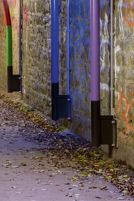 Close-up of individually colored WE-EF ZFT440 LED luminaire poles in green, blue, and purple against historic stone tunnel walls with century-old patina, each luminaire unique with customized posture—sitting, bent, or straight—creating impression of colorful light figures occupying space and communicating, three blue and two green color-filtered luminaires providing individual accents complementing 18 standard 4000K units, demonstrating WE-EF flexibility in producing customized outdoor luminaires for harsh industrial Ruhr valley environment
