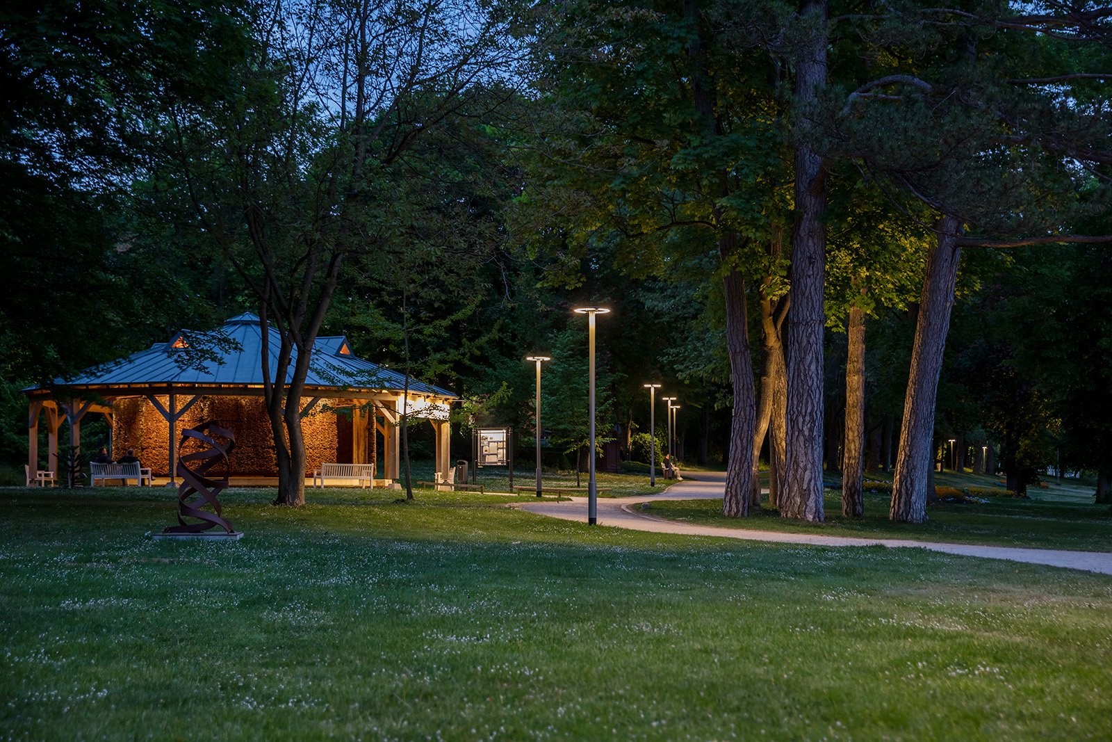 Abendliche Parklandschaft im Kurpark mit beleuchtetem Pavillon, Wegbeleuchtung und hohen Bäumen.