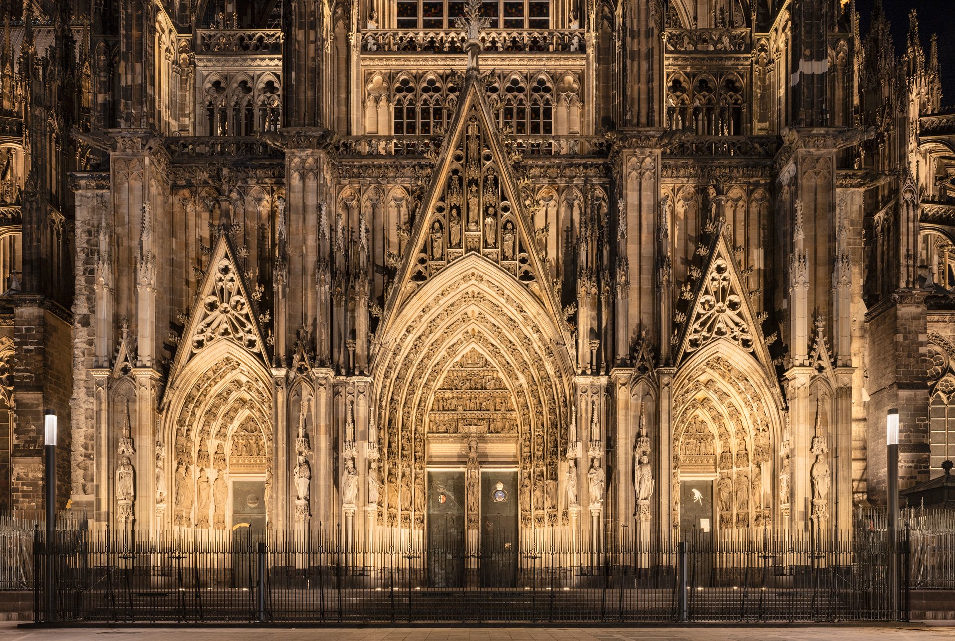 Cologne Cathedral main entrance illuminated at night with LED uplighting highlighting Gothic portal and sculptural details