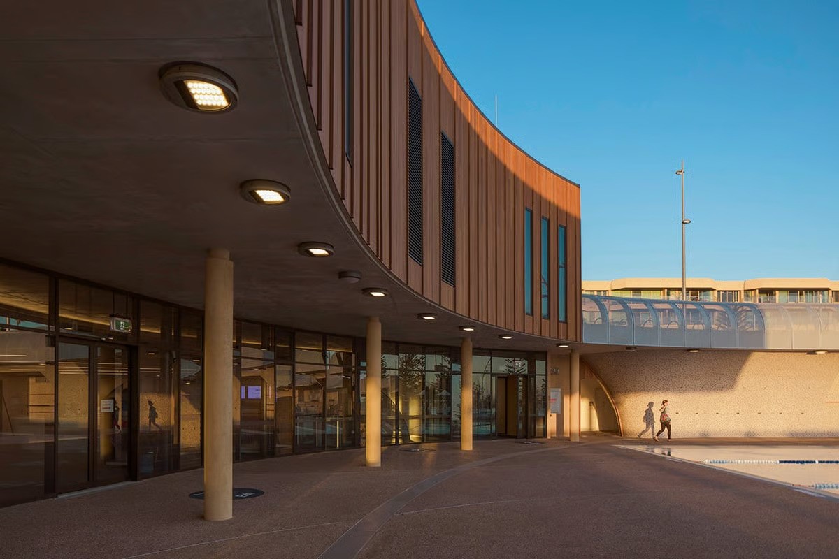 Scarborough Beach Pool entrance building with wooden cladding featuring WE-EF surface-mounted wall luminaires and sustainable architecture by Christou Design Group