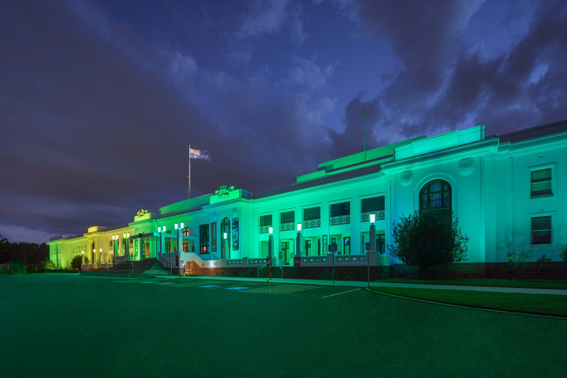 Old Parliament House showing dramatic cyan-turquoise to yellow color gradient across facade demonstrating DMX stage lighting technology allowing dynamic color progressions to sweep across building, WE-EF FLC200-CC and VLR100-CC luminaires replacing old halogen system that required manual color filter changes with efficient programmable LED solution, custom finish and DMX cable threading through heritage building's existing narrow copper conduits solved by WE-EF technical team persistence according to Integral Lighting managing director Alex Skaines
