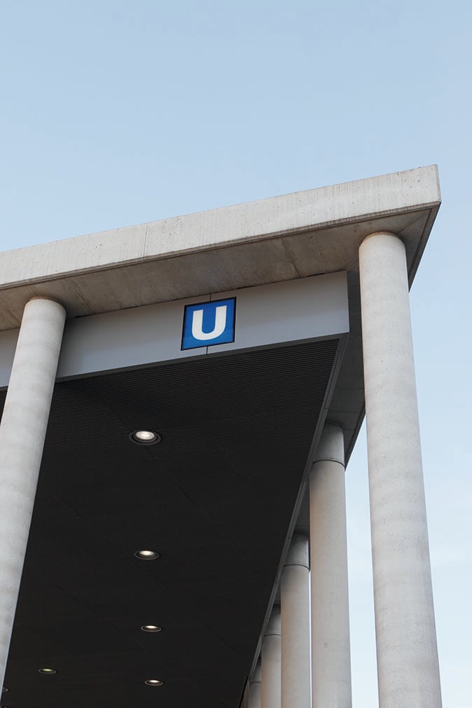 Close-up of the illuminated metro sign at the entrance to Breslauer Platz underground station in Cologne, with WE-EF recessed ceiling luminaires under the concrete canopy