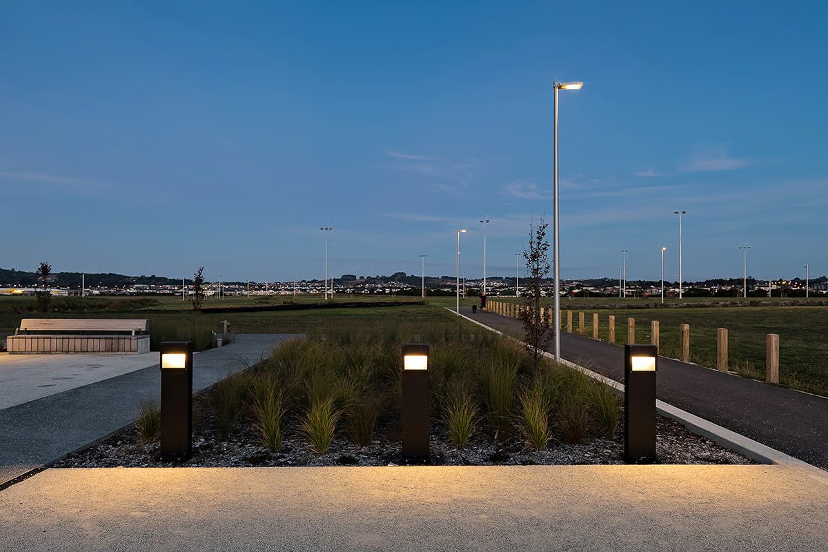 Barry Curtis Park John Walker Promenade major thoroughfare at twilight showing WE-EF STG200 recessed LED steplights in pre-cut wall openings (150 units total) and VFL520 pole-mounted luminaires with S70 streetlighting distribution lens specially designed for illuminating bike paths and footpaths at night, linking various areas of park expected to be larger than Auckland Domain when completed 2022, designed by Isthmus landscape architects with seamless collaboration between MHL and electrician onsite familiar with WE-EF products