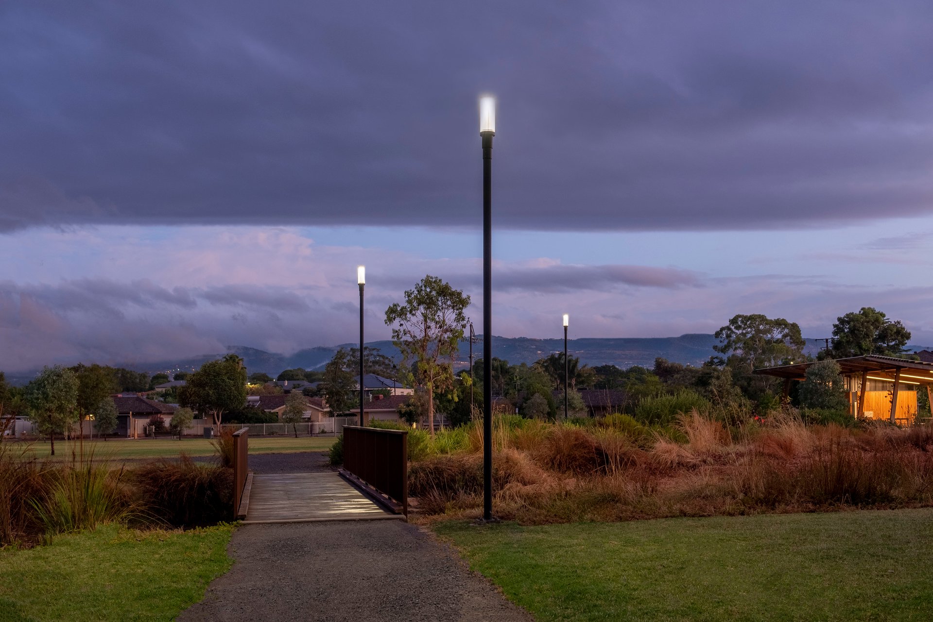 Felixstow Reserve pathway at twilight showing WE-EF ZFT400 LED luminaires balancing security lighting needs with ecological sensitivity for wildlife corridor along River Torrens/Karrawirra Parri and Fourth Creek tributaries, precise light control avoiding over-lighting concerns for adjacent residential area, sustainable LED technology with 20-30 year lifespan made from recyclable materials and fully recyclable at end-of-life, designed by Buckford Illumination Group SA for Norwood Payneham St Peters Council 2018 award-winning redevelopment