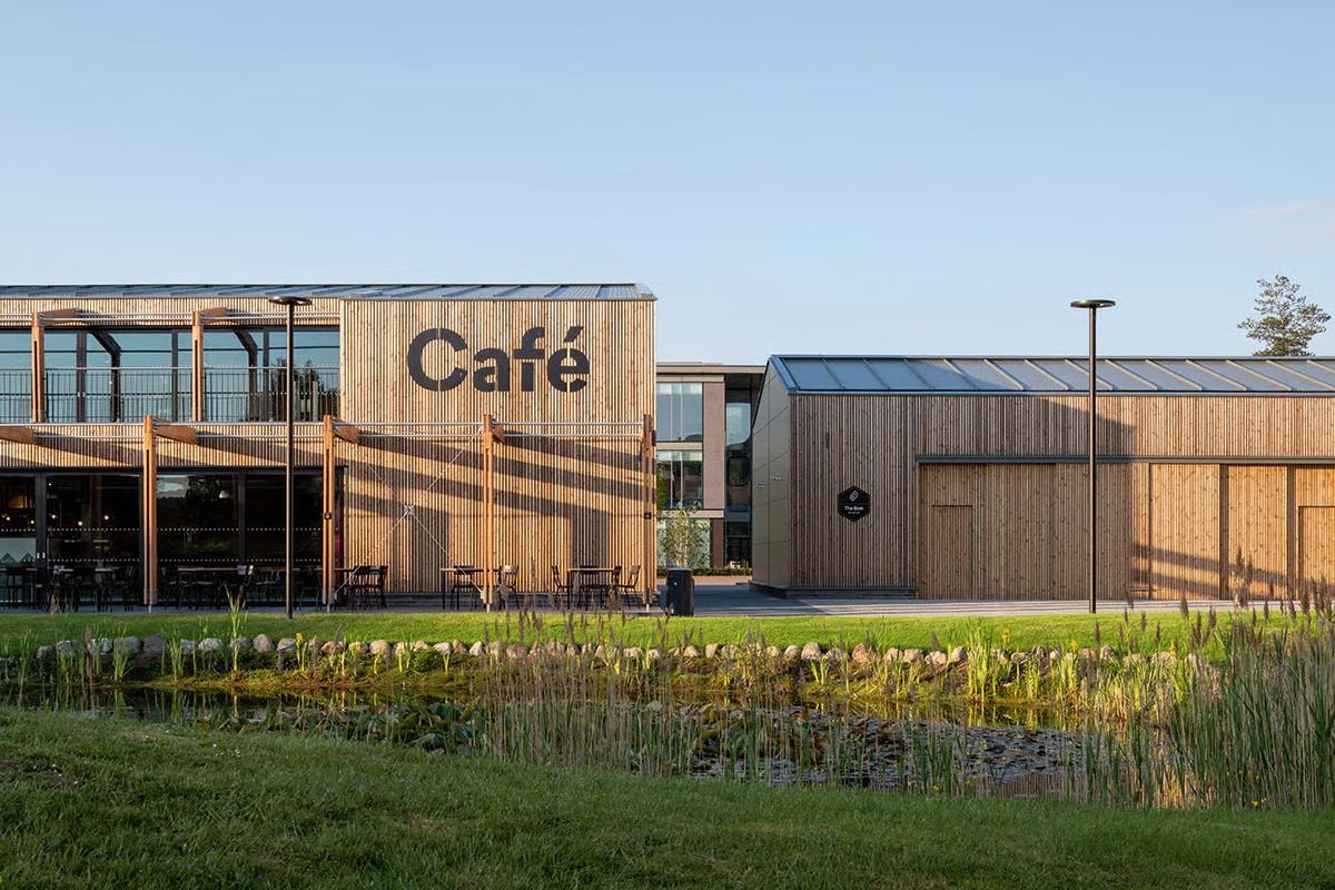 Croxley Park The Hive service centre in daylight showing contemporary architecture by ESA architects London with sustainable drainage swale landscaping, WE-EF CFT540 pole luminaires visible as defining feature of campus-like site, approximately 260 luminaires on 5-meter poles providing safe lighting for paths and open spaces, modern design supporting Columbia Threadneedle's ambitious sustainability goals for office park offering attractive working conditions for modern companies and start-ups