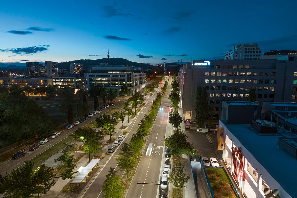Modern bus shelter on Constitution Avenue at blue hour with WE-EF LED street lighting creating safe, inviting environment along oak-lined boulevard, showcasing integration of pedestrian amenities within the Parliamentary Triangle upgrade