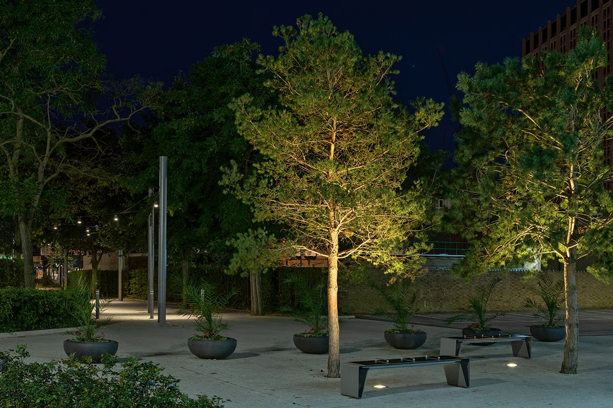 Southern House connecting pathway at evening showing WE-EF DAC220 LED downlights with warm 3000K color temperature creating pleasant lively light at comfortable brightness level, zigzag cable arrangement intuitively guiding visitors from George Street to main building entrance, spontaneous aesthetic inspired by hanging lanterns or fairy lights combined with Croydon tramline reference, mature tree naturally illuminated by functional pathway lighting