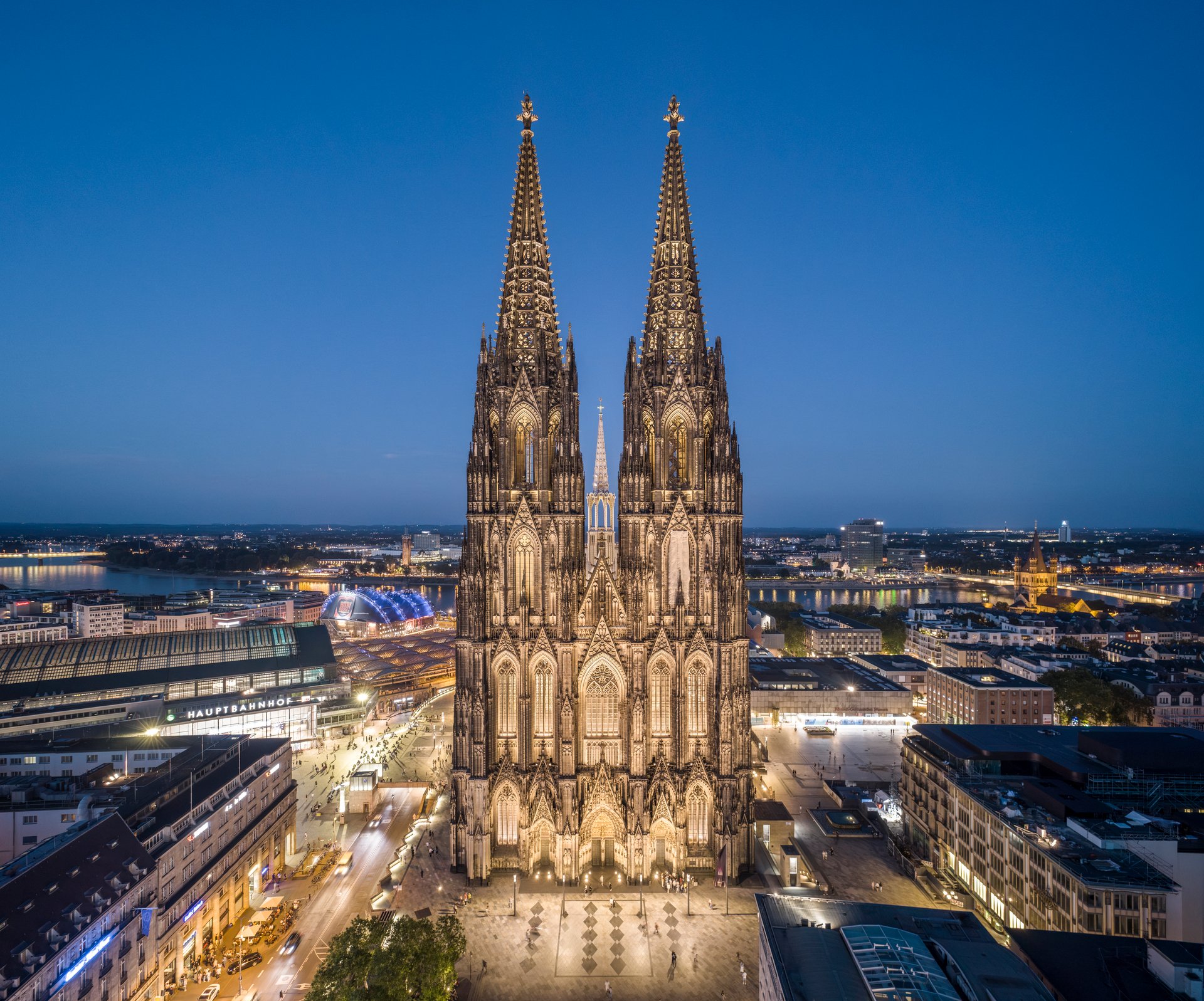 Aerial night view of illuminated Cologne Cathedral dominating the cityscape with Rhine River and surrounding urban environment
