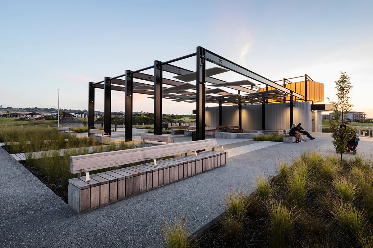 Barry Curtis Park pavilion changing room facility in daylight showing contemporary layered ceiling design with WE-EF FLC100 LED projectors creating dramatic shadow play, multiple design awards recognition, part of vast multi-user facility completed over 13-14 year period following 2008 global financial crisis delays, comprehensive lighting solution by MHL Auckland consultant Jayden Cocker for Auckland Council including VFL520 pole-mounted luminaires, ETV100 linear uplights, and ecologically-themed playground lighting