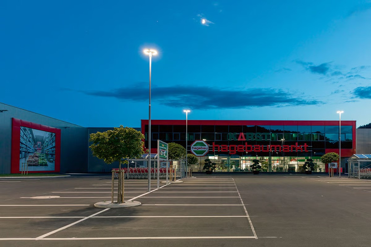 WE-EF CFT540 car park lighting at dusk providing 25 lux average illuminance at Hagebaumarkt Kronach KfW Efficiency House 55 building with LED exterior lighting