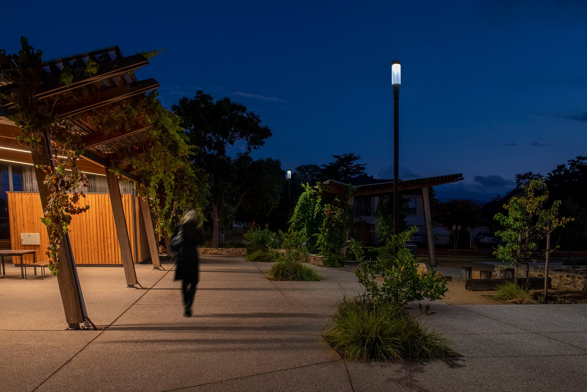 Felixstow Reserve pathway at blue hour with silhouetted walker beneath WE-EF ZFT400 lantern-style LED luminaire, demonstrating secure evening environment created through careful lighting design avoiding over-lighting concerns for dense residential area backing onto reserve, part of award-winning redevelopment celebrating Indigenous custodians' traditional use of land and providing great outcome for broader Adelaide community