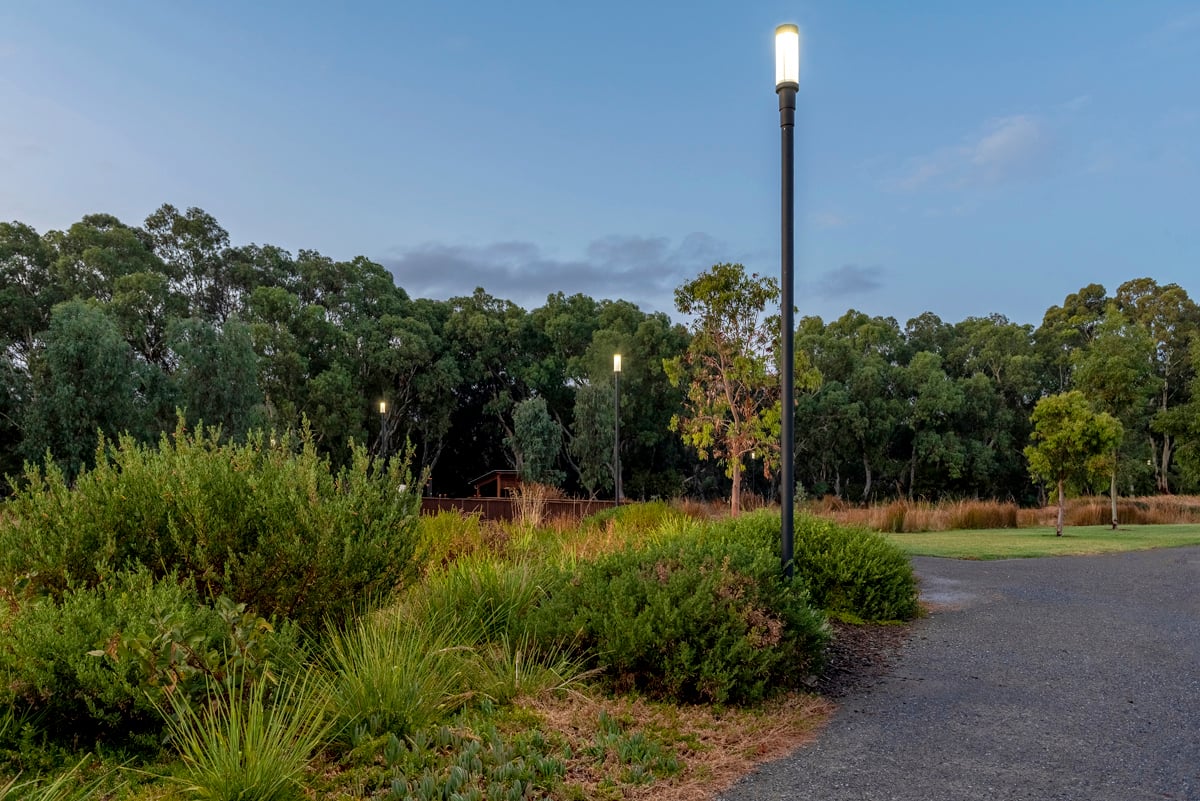 Felixstow Reserve pathway in daylight showing WE-EF ZFT400 street and area luminaire with circular form sitting directly on pole rather than extending from arm, native Australian landscaping by ASPECT Studios and Oxigen flanking shared path, luminaire selected for quality, LED longevity advantages, precise light control with asymmetric or rectangular side-throw distributions providing pathway solution with very limited backward light to protect residential neighbors