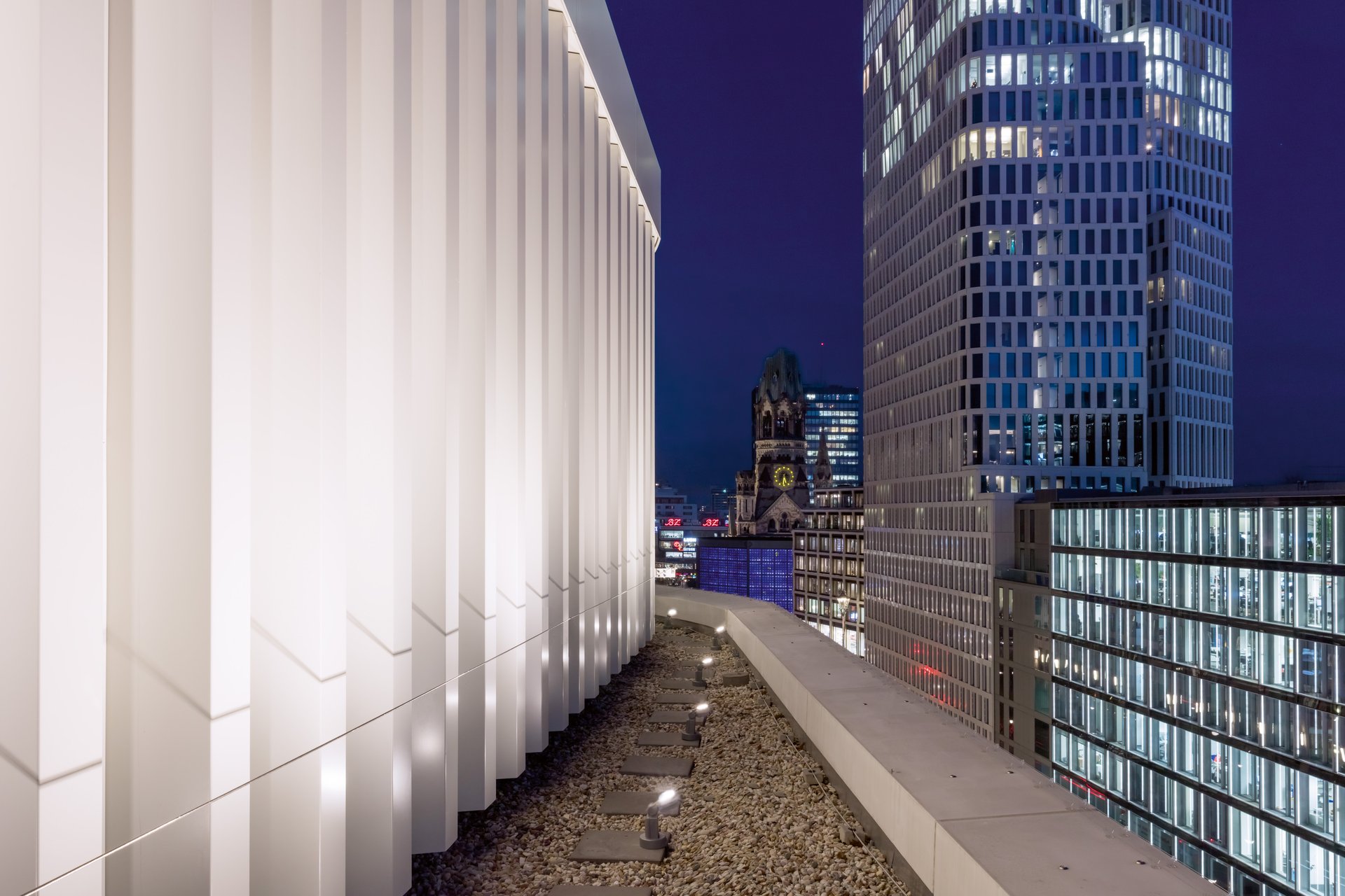 Zoom Berlin rooftop terrace with WE-EF inground lighting illuminating vertical architectural elements overlooking Kaiser Wilhelm Memorial Church at dusk