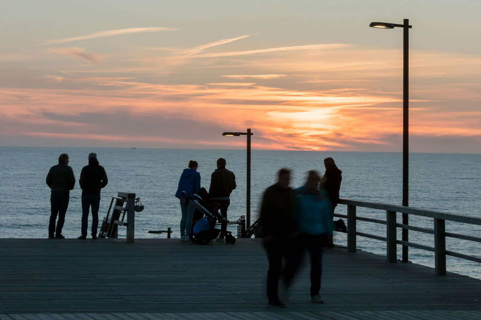 Des personnes admirent le coucher de soleil depuis la plateforme panoramique de l'escalier de plage de Wenningstedt, sur l'île de Sylt, éclairée par des luminaires sur mât WE-EF
