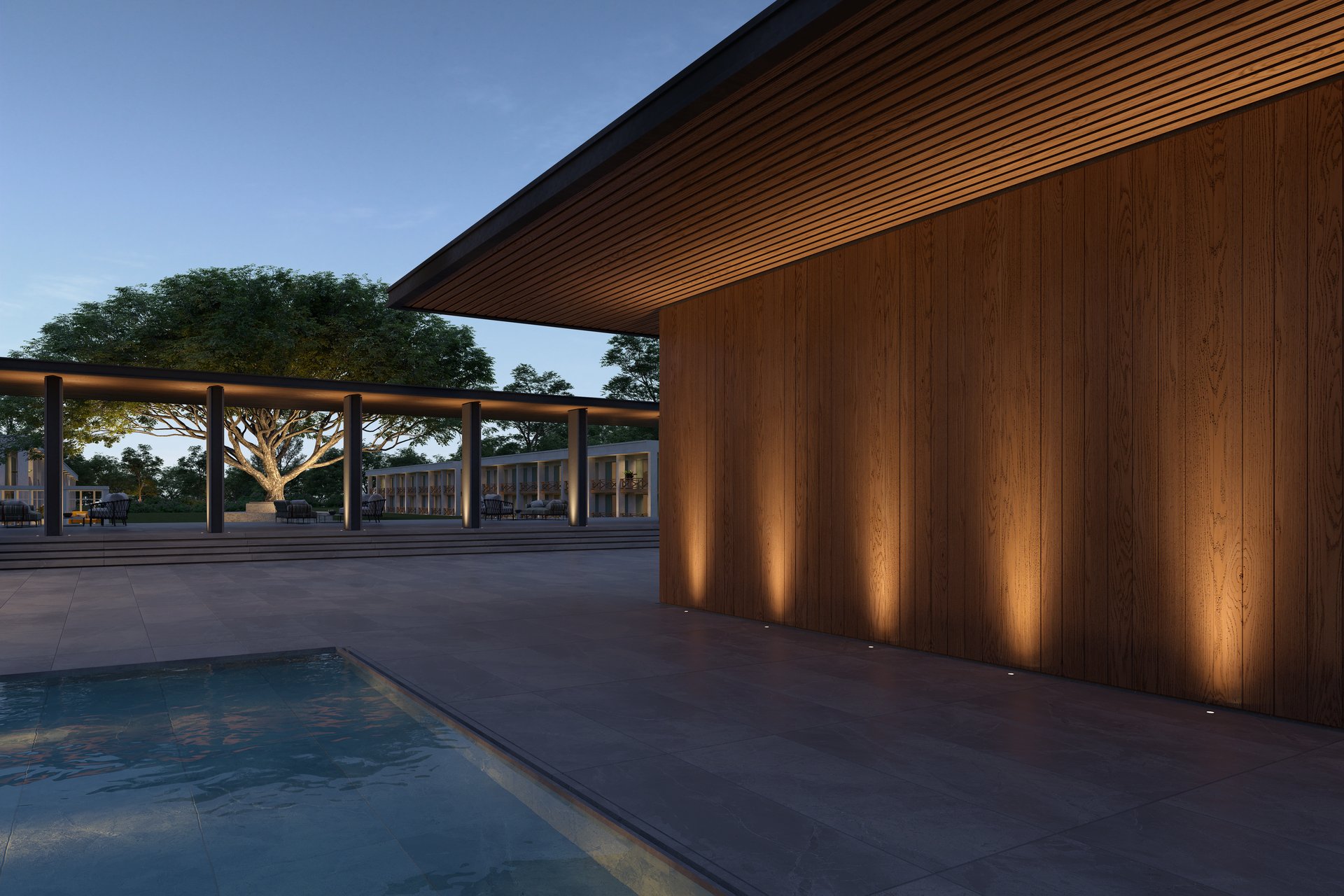 Contemporary hotel or resort complex at dusk featuring architectural outdoor lighting. In-ground luminaires illuminate a timber-clad façade with warm light, while a large tree and surrounding building structures are subtly highlighted. A reflecting pool in the foreground enhances the calm and premium atmosphere of the setting.
