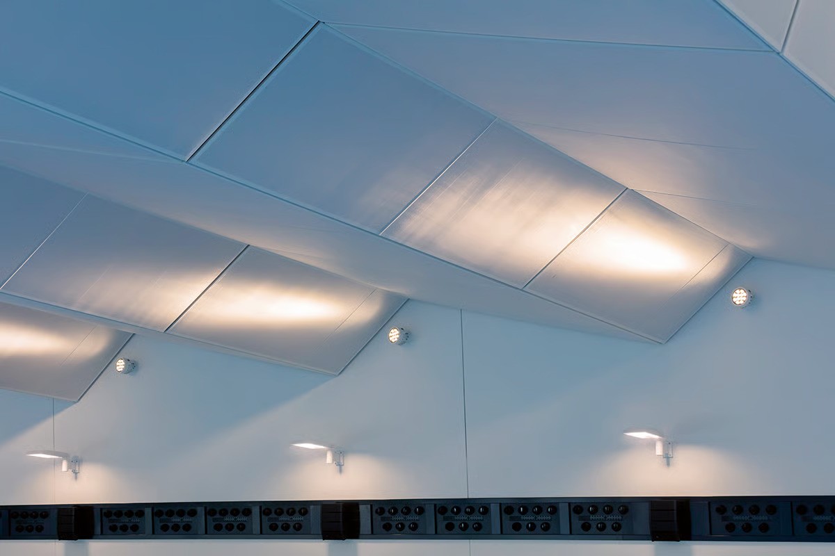 Detail of Hamburg-Ohlsdorf swimming pool folded membrane ceiling with light textile acoustic elements illuminated from both sides by WE-EF FLC230 projectors creating uniform bright atmosphere, innovative ceiling design concealing wooden truss structure, lighting trial on-site determined optimal combination of narrow-beam LED optics and linear spread lens for desired grazing effect, DALI interface enabling programmable lighting scenarios for different pool activities