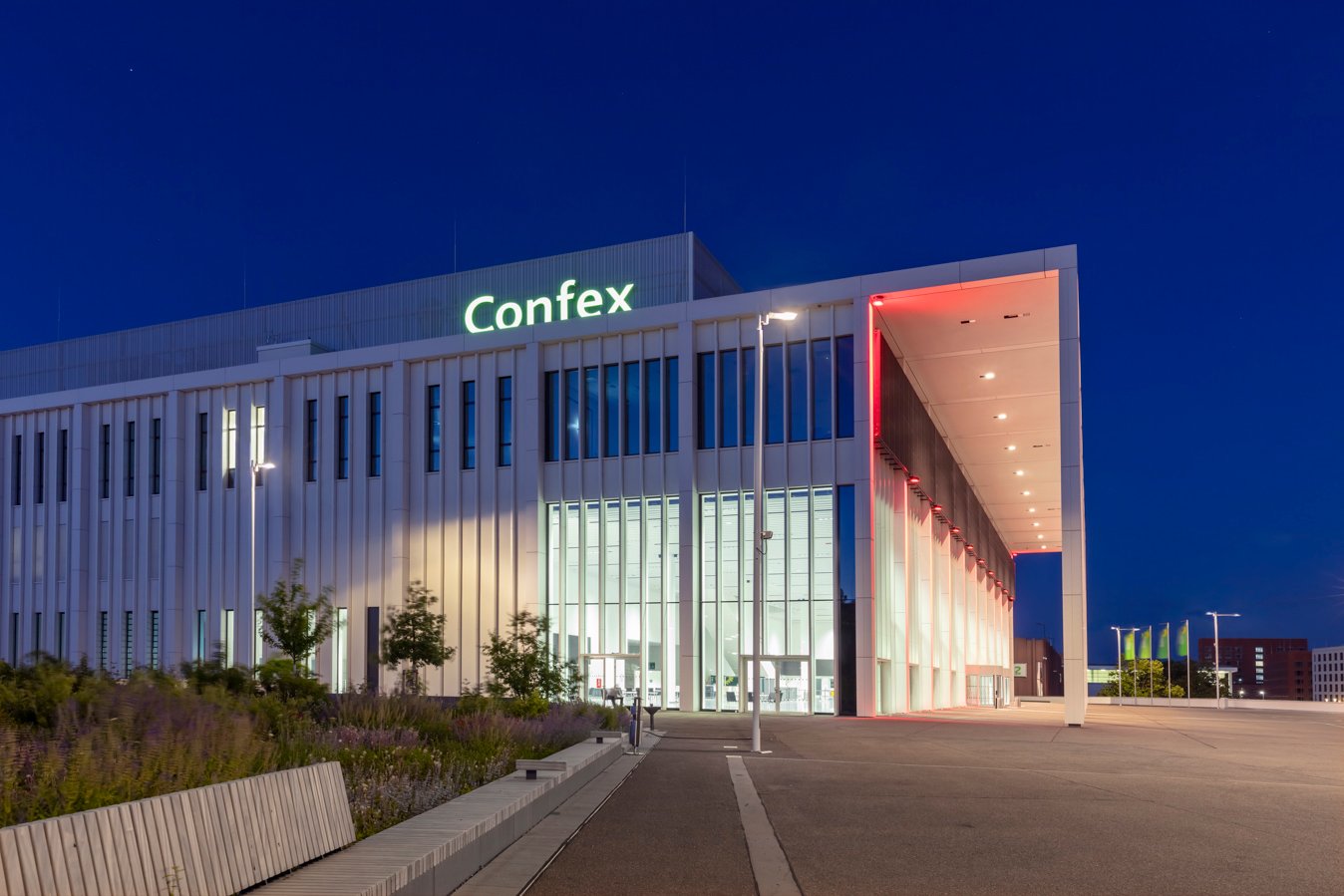 Modernes Gebäude mit beleuchteter Fassade und großem Eingangsbereich bei Nacht.